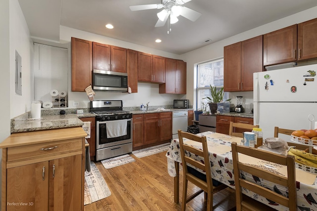 kitchen with sink, ceiling fan, stainless steel appliances, light stone countertops, and light hardwood / wood-style flooring