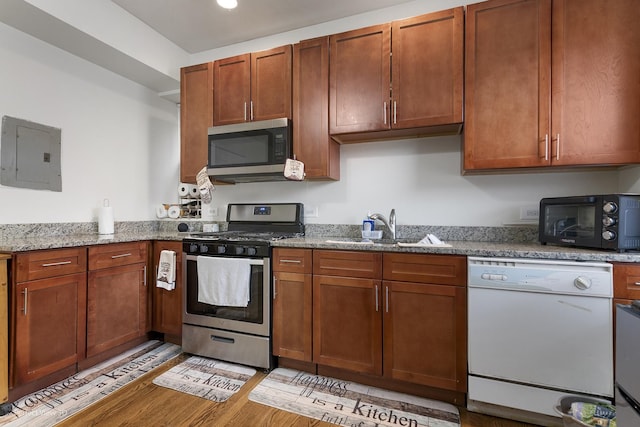 kitchen with sink, electric panel, stainless steel appliances, light stone countertops, and light hardwood / wood-style flooring