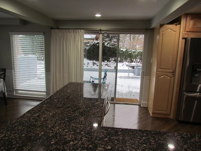 kitchen featuring dark wood-type flooring, dark stone counters, and stainless steel fridge