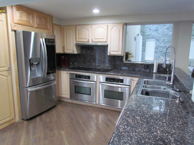 kitchen featuring sink, stainless steel appliances, dark hardwood / wood-style floors, tasteful backsplash, and dark stone counters