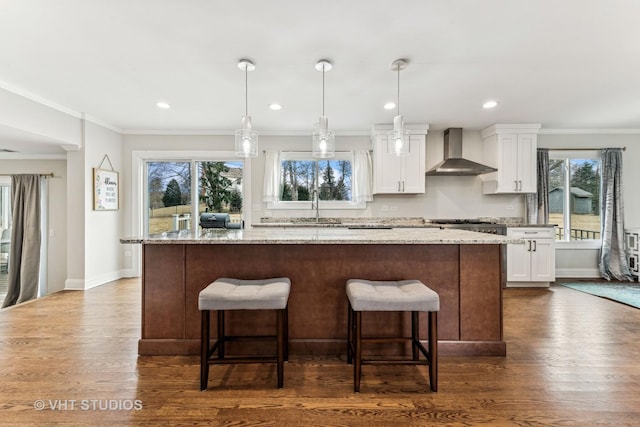 kitchen featuring light stone counters, wall chimney exhaust hood, a kitchen island, and white cabinets