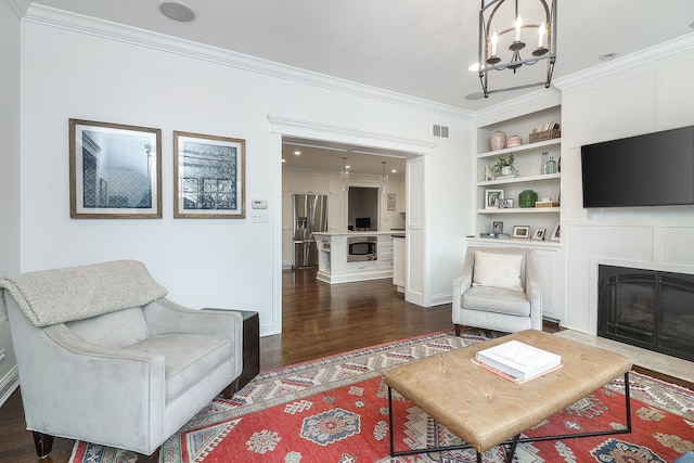 living room featuring dark hardwood / wood-style flooring, built in features, ornamental molding, and an inviting chandelier