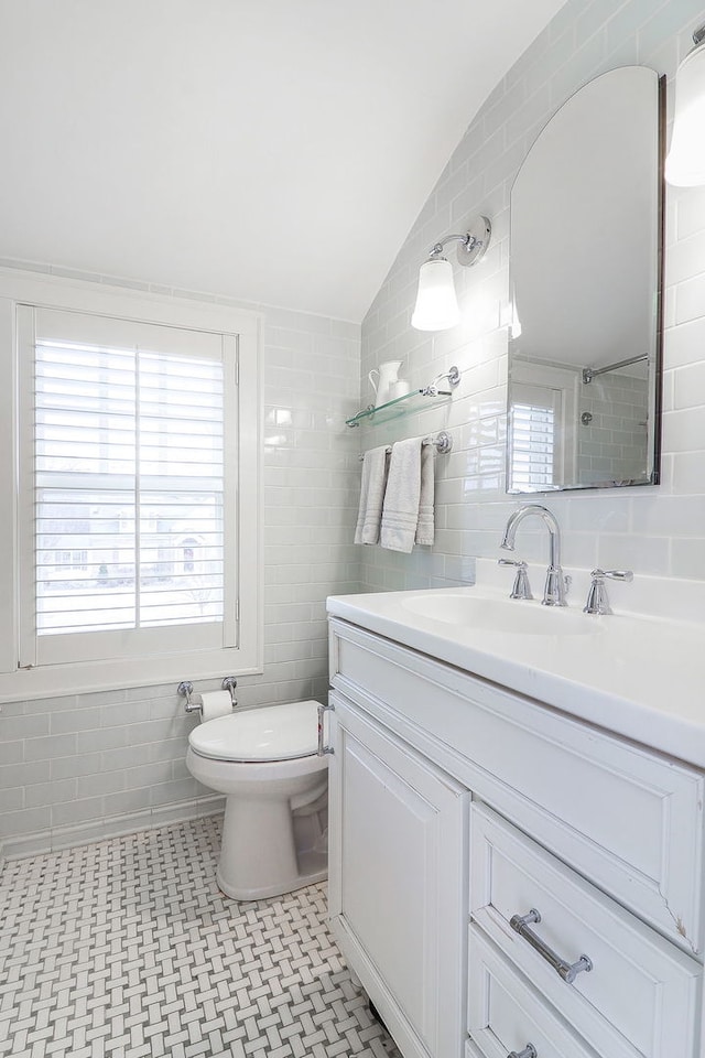 bathroom with tile walls, vanity, vaulted ceiling, and toilet