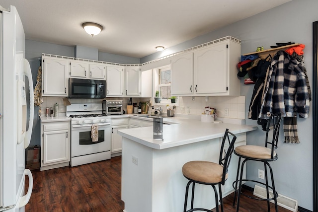 kitchen with white cabinetry, white appliances, a breakfast bar, and kitchen peninsula