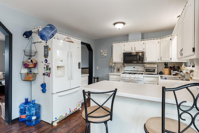 kitchen with sink, white appliances, white cabinets, a kitchen bar, and kitchen peninsula