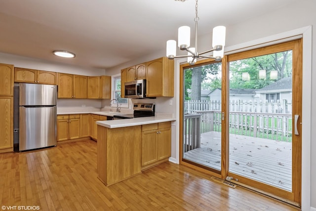 kitchen featuring stainless steel appliances, a peninsula, a sink, light countertops, and light wood-type flooring