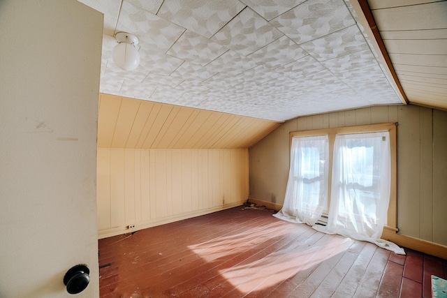 additional living space with hardwood / wood-style flooring, vaulted ceiling, and wooden walls