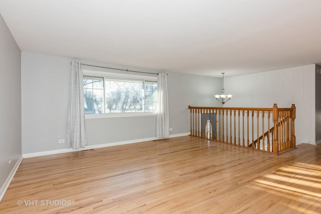 spare room featuring light wood-type flooring, visible vents, a chandelier, and baseboards