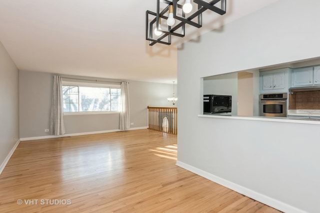 unfurnished living room featuring a chandelier, light wood finished floors, and baseboards