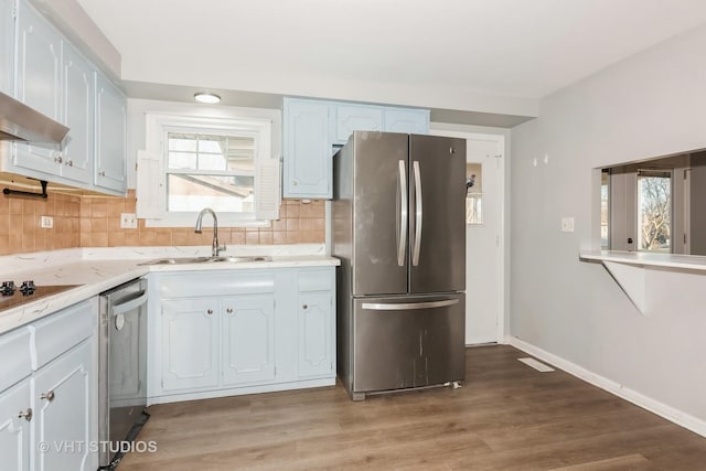 kitchen featuring backsplash, appliances with stainless steel finishes, light wood-style floors, a sink, and baseboards