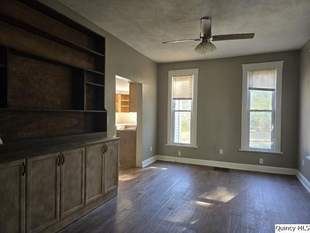 unfurnished living room featuring dark wood-type flooring, ceiling fan, and built in shelves