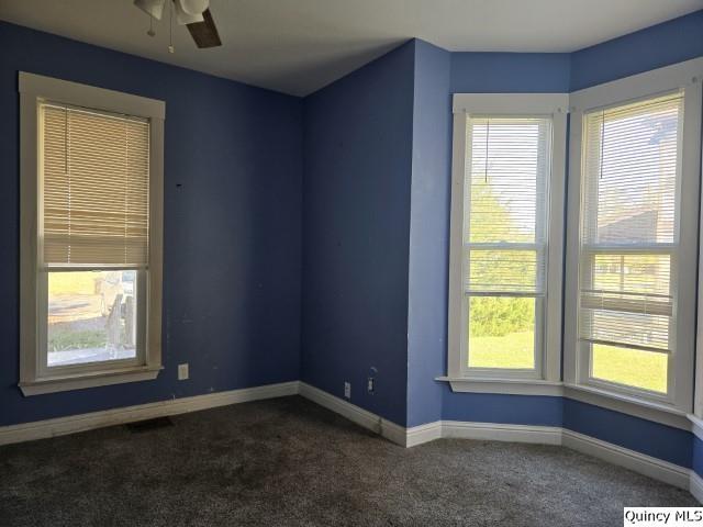 spare room with ceiling fan and dark colored carpet