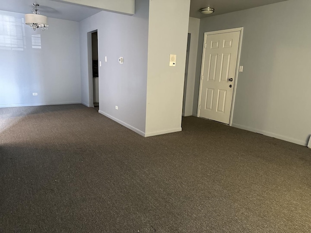 unfurnished room with a chandelier, dark carpet, and baseboards