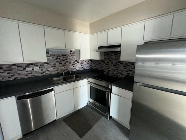 kitchen featuring white cabinets, dark countertops, stainless steel appliances, under cabinet range hood, and a sink