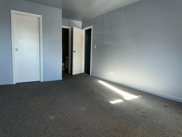 unfurnished bedroom with dark carpet and baseboards