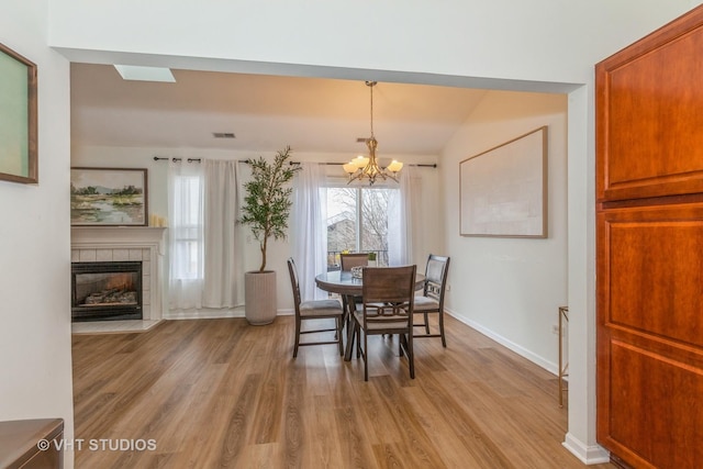 dining room with a tiled fireplace, light hardwood / wood-style flooring, and a notable chandelier