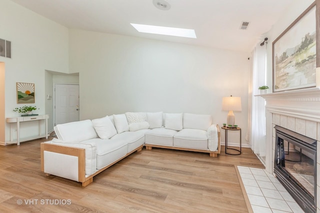 living room featuring a tile fireplace, vaulted ceiling with skylight, and light wood-type flooring