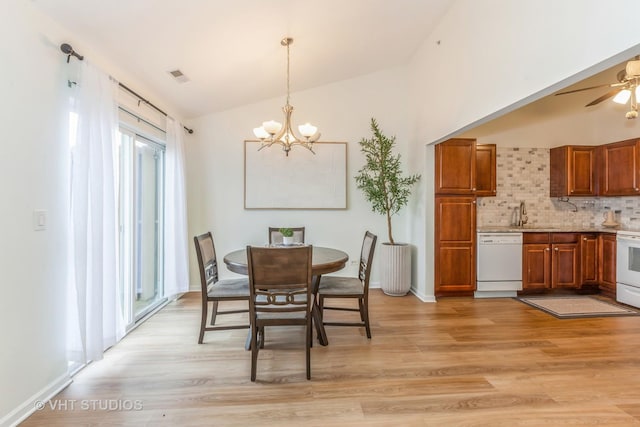 dining space with vaulted ceiling, sink, ceiling fan with notable chandelier, and light hardwood / wood-style flooring