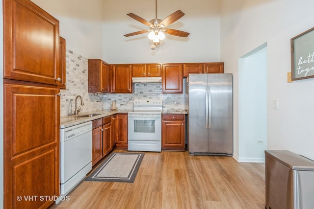 kitchen featuring sink, light wood-type flooring, decorative backsplash, a high ceiling, and white appliances