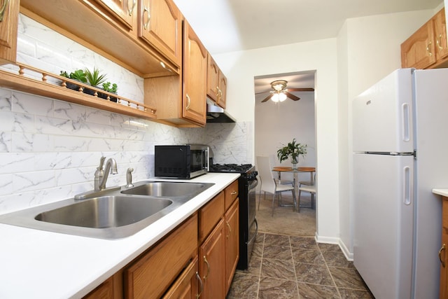 kitchen featuring black gas range oven, sink, backsplash, white refrigerator, and exhaust hood