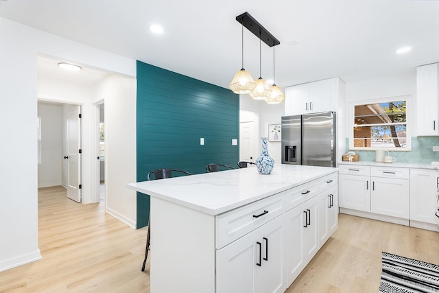 kitchen with stainless steel refrigerator with ice dispenser, a breakfast bar area, a center island, light stone countertops, and white cabinets