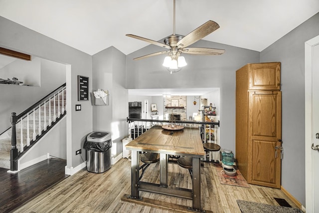 dining area featuring vaulted ceiling, a large fireplace, ceiling fan, and light hardwood / wood-style flooring