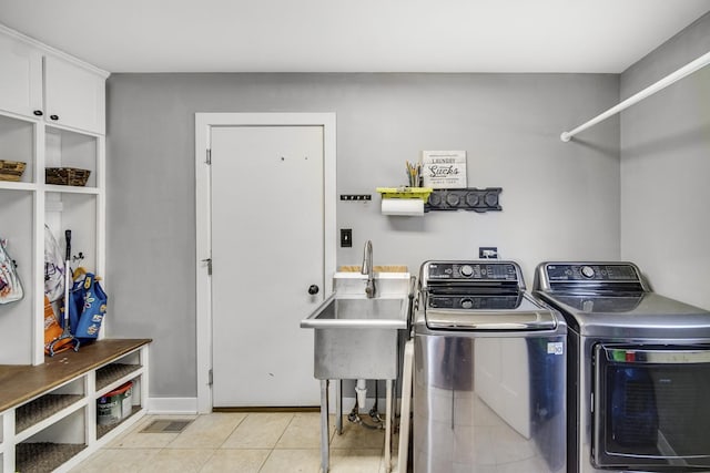 clothes washing area with cabinets, sink, washer and dryer, and light tile patterned floors