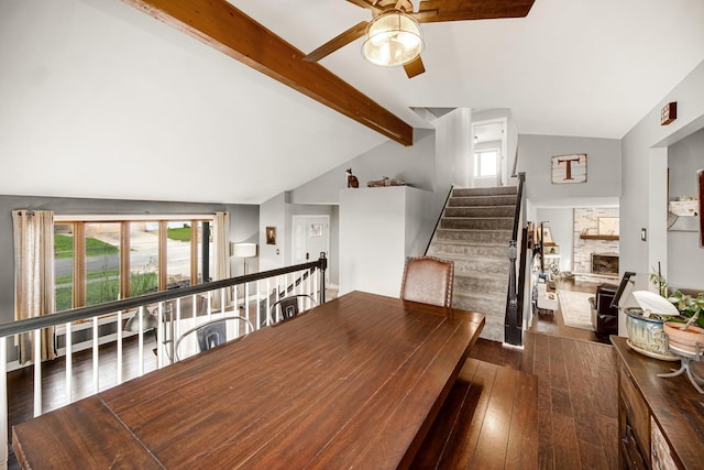 dining area with lofted ceiling with beams, ceiling fan, dark wood-type flooring, and a fireplace