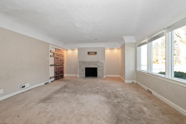 unfurnished living room with a high end fireplace, light carpet, and a textured ceiling