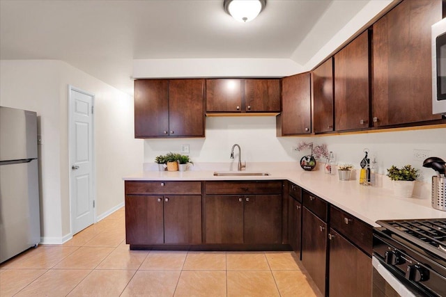 kitchen featuring appliances with stainless steel finishes, sink, light tile patterned floors, and dark brown cabinets