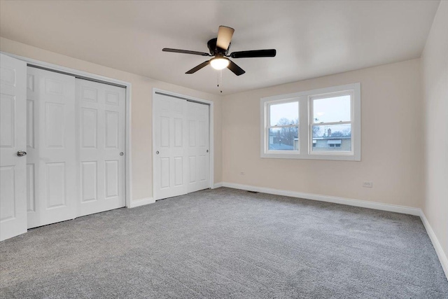 unfurnished bedroom with ceiling fan, carpet flooring, and two closets