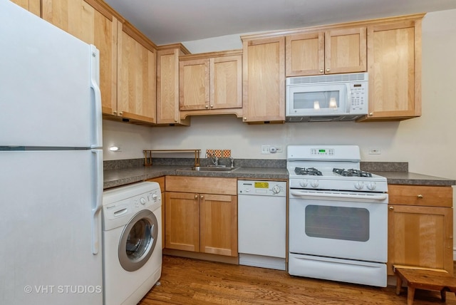 kitchen with white appliances, dark countertops, washer / clothes dryer, wood finished floors, and a sink