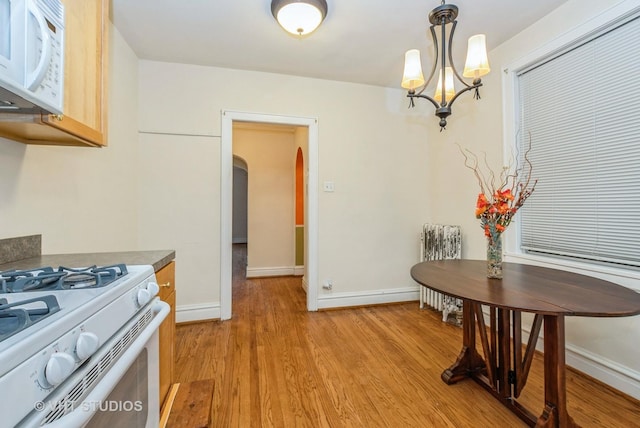 kitchen featuring arched walkways, decorative light fixtures, light wood-type flooring, white appliances, and baseboards