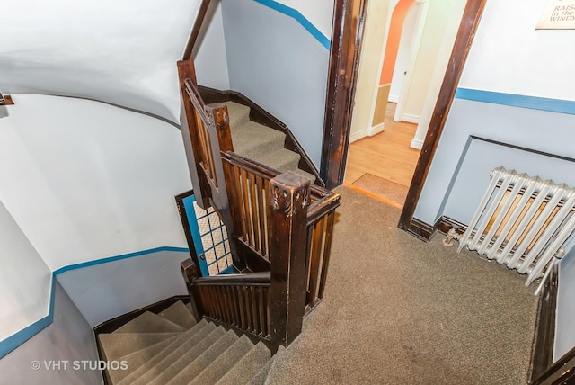 staircase with arched walkways, radiator heating unit, carpet flooring, and baseboards