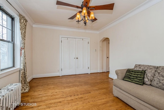 living area featuring arched walkways, light wood finished floors, radiator heating unit, ornamental molding, and baseboards