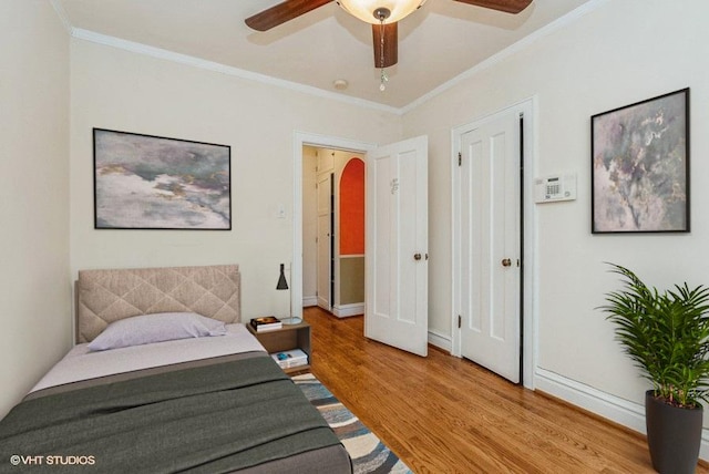 bedroom featuring arched walkways, light wood finished floors, baseboards, and crown molding