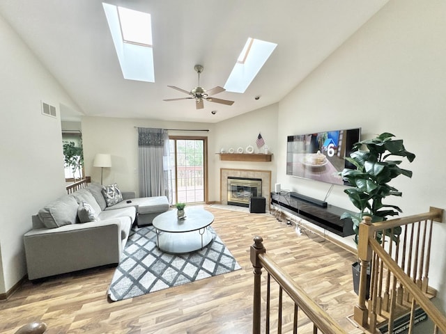 living room with lofted ceiling with skylight, a tiled fireplace, and hardwood / wood-style floors