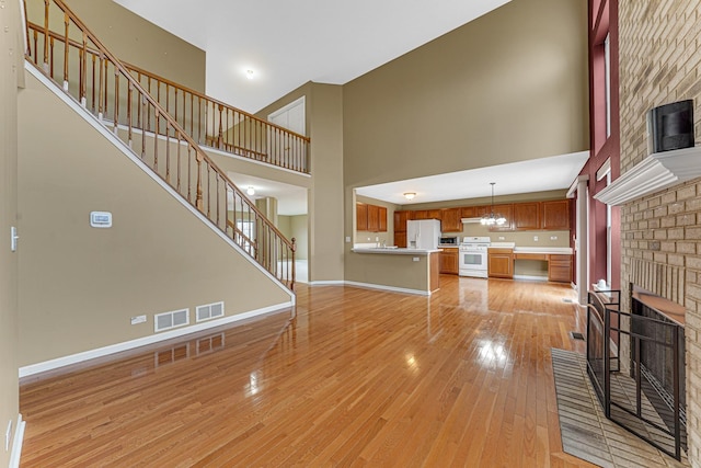 unfurnished living room featuring a brick fireplace, a towering ceiling, a chandelier, and light hardwood / wood-style flooring