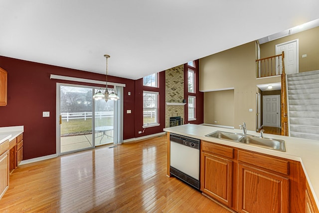 kitchen featuring sink, light wood-type flooring, dishwasher, pendant lighting, and a fireplace