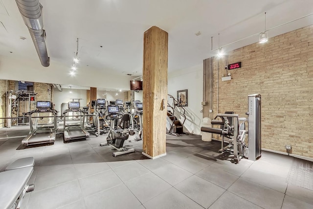 exercise room featuring rail lighting and brick wall