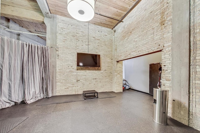 unfurnished living room featuring a towering ceiling, brick wall, and wooden ceiling