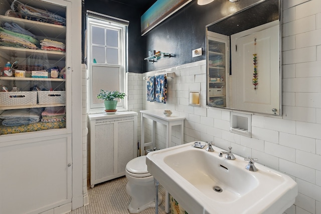 bathroom with radiator, sink, tile walls, toilet, and tile patterned floors