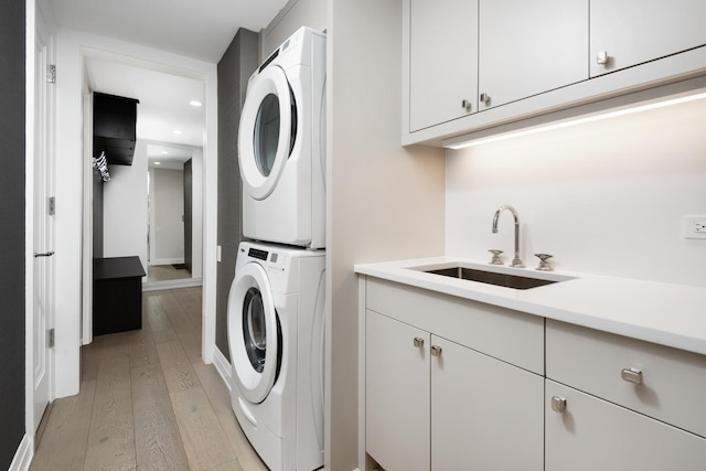 clothes washing area featuring cabinets, stacked washing maching and dryer, sink, and light wood-type flooring