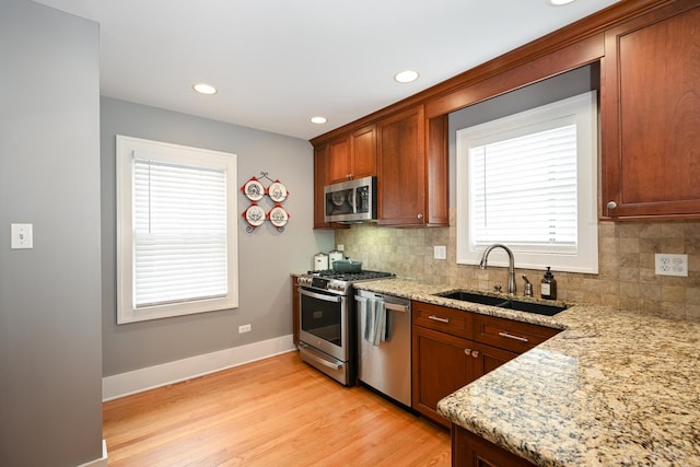 kitchen with tasteful backsplash, sink, light stone counters, stainless steel appliances, and light hardwood / wood-style flooring