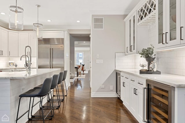 kitchen with white cabinets, light stone countertops, pendant lighting, and beverage cooler