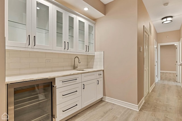 bar featuring wine cooler, light wood-type flooring, white cabinets, light stone countertops, and backsplash