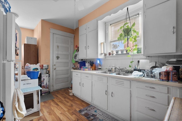 kitchen with sink, white cabinets, light wood-type flooring, and decorative backsplash