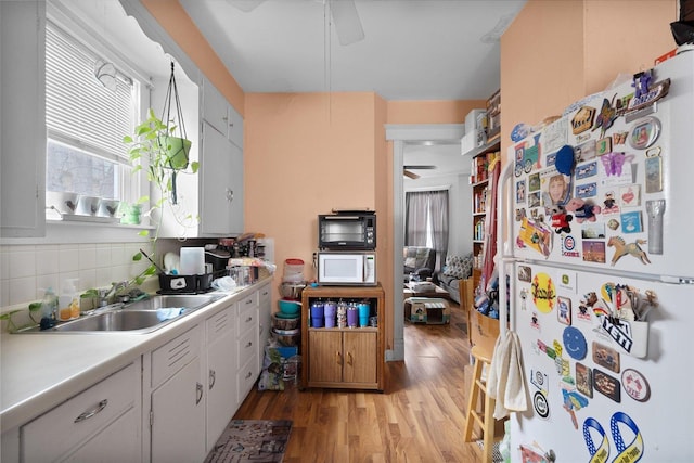 kitchen with sink, white appliances, light hardwood / wood-style flooring, white cabinetry, and tasteful backsplash