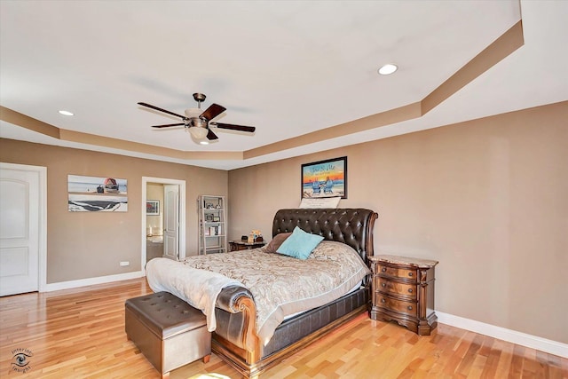 bedroom featuring connected bathroom, hardwood / wood-style floors, a raised ceiling, and ceiling fan