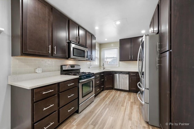 kitchen featuring dark brown cabinetry, light wood finished floors, stainless steel appliances, and a sink